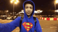 a young man wearing a blue superman hoodie takes a selfie