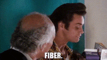 two men are sitting next to each other in a room and one of them is talking about fiber .