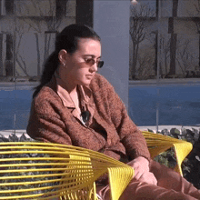 a woman wearing sunglasses is sitting on a yellow chair .