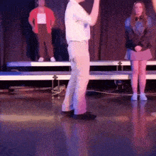 a man in a white shirt is standing on a stage with a woman in a red jacket behind him