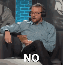 a man wearing headphones and glasses is sitting on a couch holding a notebook and the word no is visible
