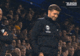 a man wearing an american express jacket gives a thumbs up in front of a crowd