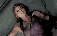 a woman in a purple tank top is laying on the ground with blood coming out of her mouth .