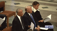 a man in a suit sits next to a woman holding a piece of paper and a sign that says c span
