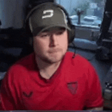 a man wearing headphones and a baseball cap is sitting in front of a computer screen .