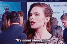 a woman is standing in front of a crowd of people and talking about bloody time .