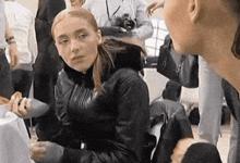 a woman in a black leather jacket is sitting on the floor talking to another woman in a crowd .