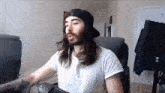 a man with long hair and a beard is wearing a hat and headphones while sitting in a chair .