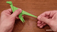 a person is holding a green origami dinosaur made in animonica