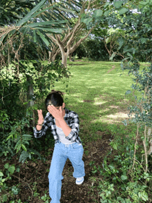 a woman in a plaid shirt covering her face in a park