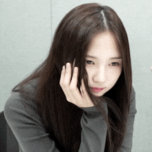 a woman with long dark hair holds her hand to her head