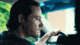 a man is sitting in the driver 's seat of a car and pointing at something .