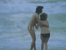 a man and a woman in bikinis are hugging on a beach