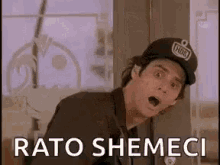 a man wearing a baseball cap is standing in front of a window with his mouth open and says rato shemeci .