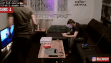 a man sitting on a couch with a sign that says support liverpool behind him