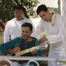a man is playing a guitar while another man watches