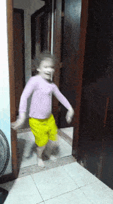 a little girl in yellow shorts and a purple shirt is dancing in a hallway