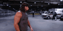 a man in a tank top is standing in a parking lot with ambulance 's in the background .