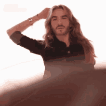 a man with long hair and a beard is holding his hand to his head