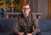a man wearing glasses is sitting on a blue couch looking at his phone
