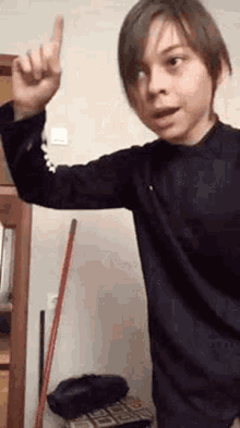 a young boy is pointing up with his finger while standing in front of a mop .