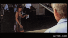 a woman in a gray dress is walking towards a man in a blue shirt with gifrun.com below her