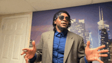 a man in a suit and sunglasses is standing in front of a wall with a picture of a city skyline