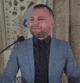 a man in a blue suit stands at a podium with a microphone