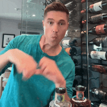 a man in a blue shirt is standing in front of a wall of wine bottles and a bottle with the letter r on it