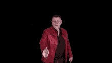 a man in a red leather jacket is holding a gun in front of a hole in the wall .
