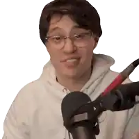 a man wearing glasses and a white hoodie is standing in front of a microphone