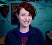a woman with red hair is smiling in front of a wall with a shield that says ' a ' on it