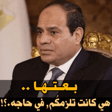 a man in a suit and tie sits in a chair with arabic writing above him