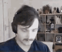 a man with a mustache is wearing headphones and looking at the camera in a living room .