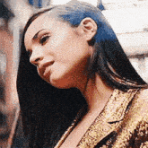 a close up of a woman 's face with long black hair wearing a gold jacket and earrings .