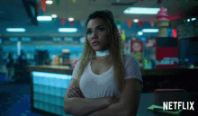 a woman is sitting at a table with her arms crossed and a netflix logo in the corner