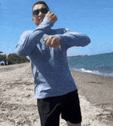 a man wearing sunglasses and a blue shirt is standing on the beach looking at his watch