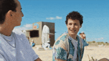 two young men are sitting on a beach and talking to each other