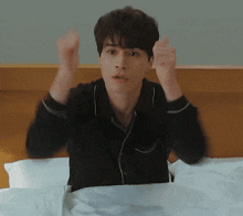 a man in a black shirt is sitting on a bed with his arms in the air