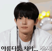 a young man with black hair and a white shirt is looking at the camera with a serious look on his face .