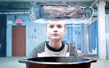 a woman is sitting in front of a pot of water with a glass bowl on her head .