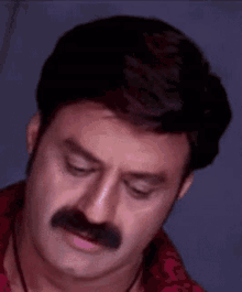 a man with a mustache and a red shirt is looking down .
