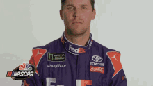 a man in a purple and orange racing suit is standing in front of a white wall .