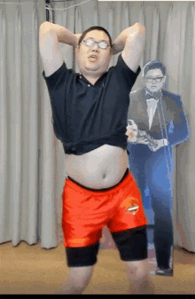 a man in a black shirt and orange shorts stands in front of a cardboard cutout of kim jong un