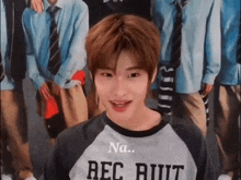 a young man wearing a shirt that says rec ruiit is standing in front of a group of people .