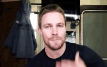 a man with a beard is wearing a black shirt and giving a thumbs up