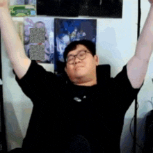 a man wearing glasses and a black shirt is raising his arms in the air .