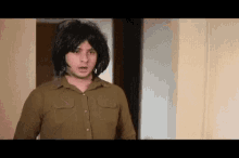 a man wearing a wig and a brown shirt is standing in a room .
