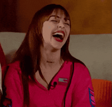 a woman in a pink shirt is laughing with her mouth open while sitting on a couch .