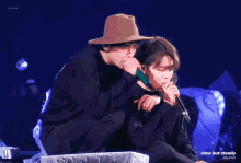 a man in a hat is hugging another man while holding a microphone
